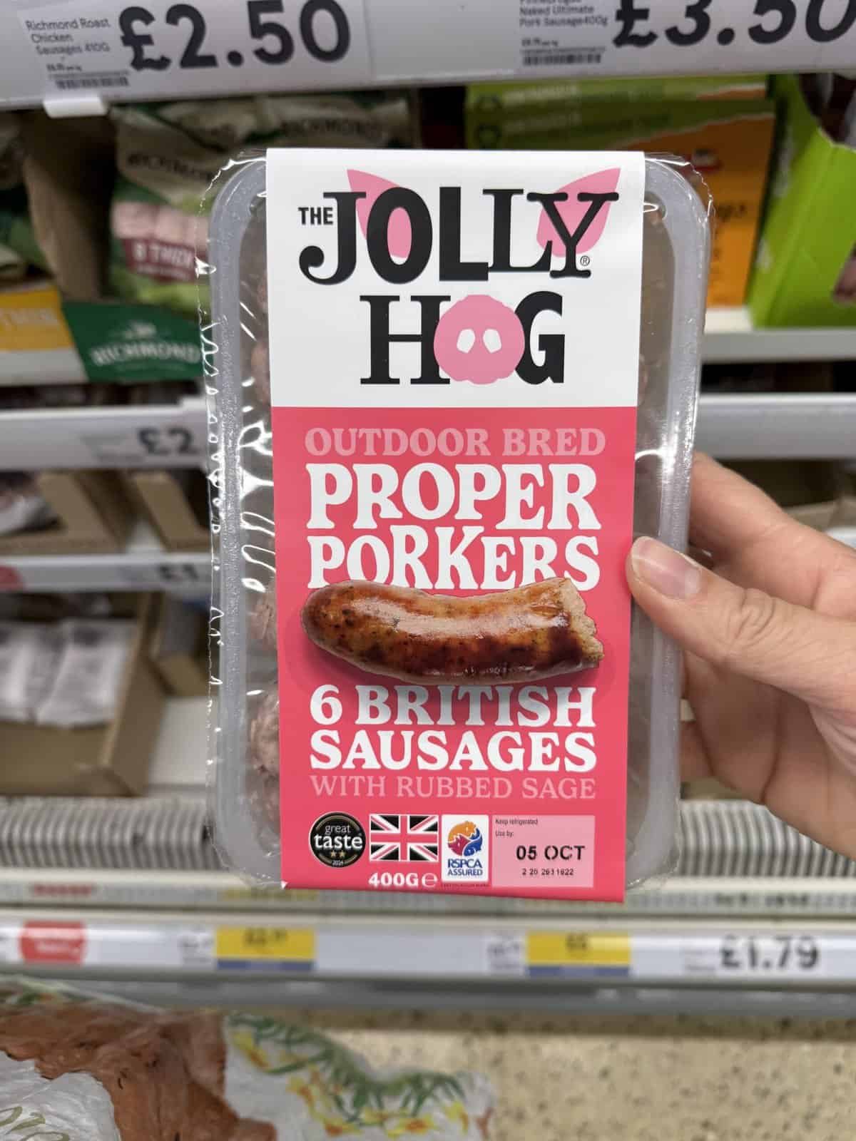 Hand holding a pack of Jolly Hog sausages.