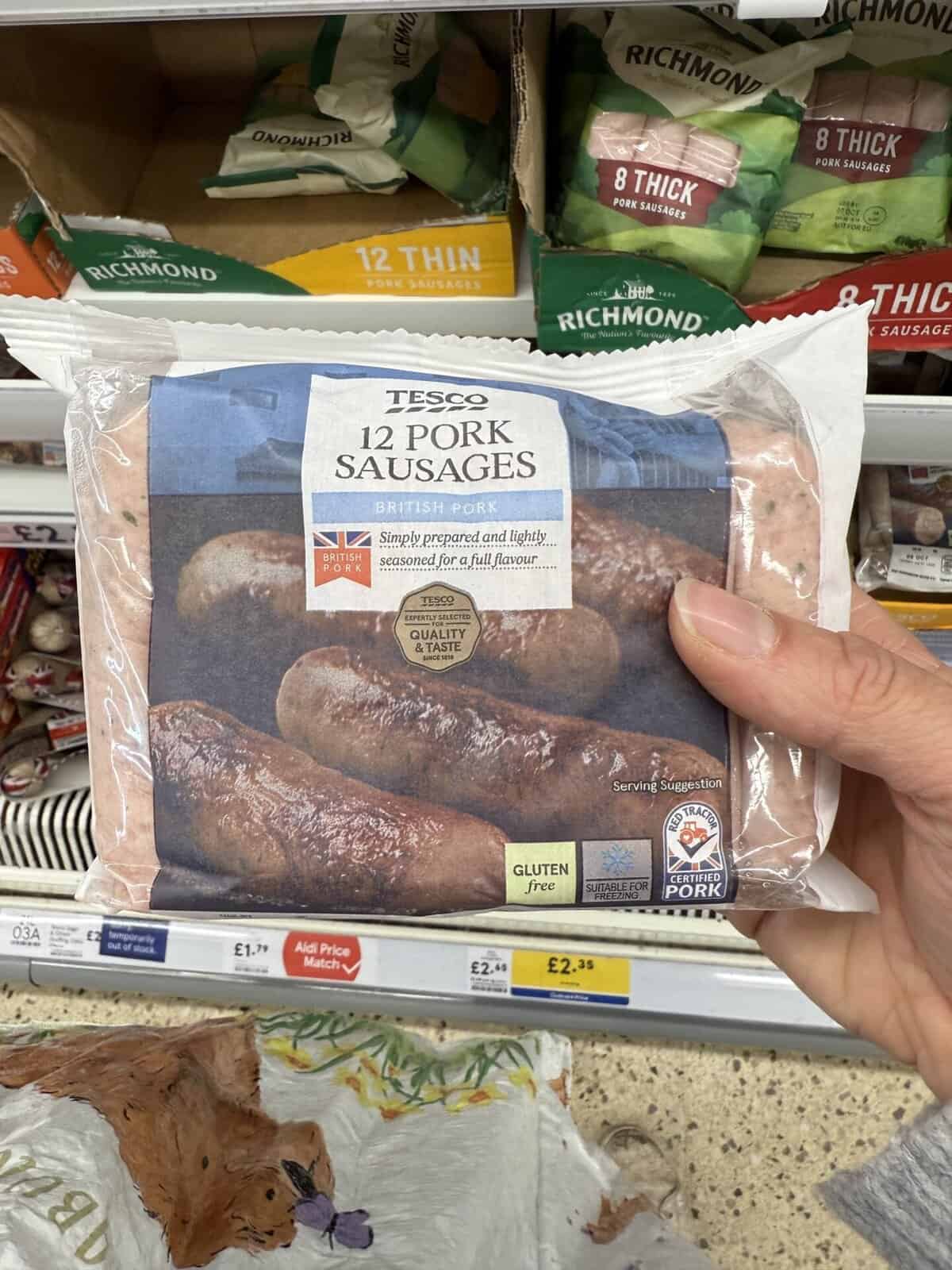 Hand holding a pack of Tesco pork sausages which are gluten free.