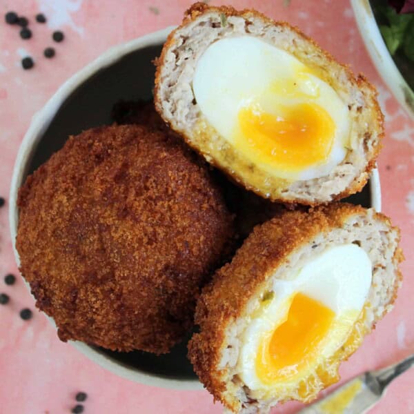 A bowl with gluten free scotch eggs in, with one cut in half to show a jammy yolk.