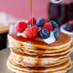 A stack of gluten free American pancakes with yoghurt, berries and syrup.