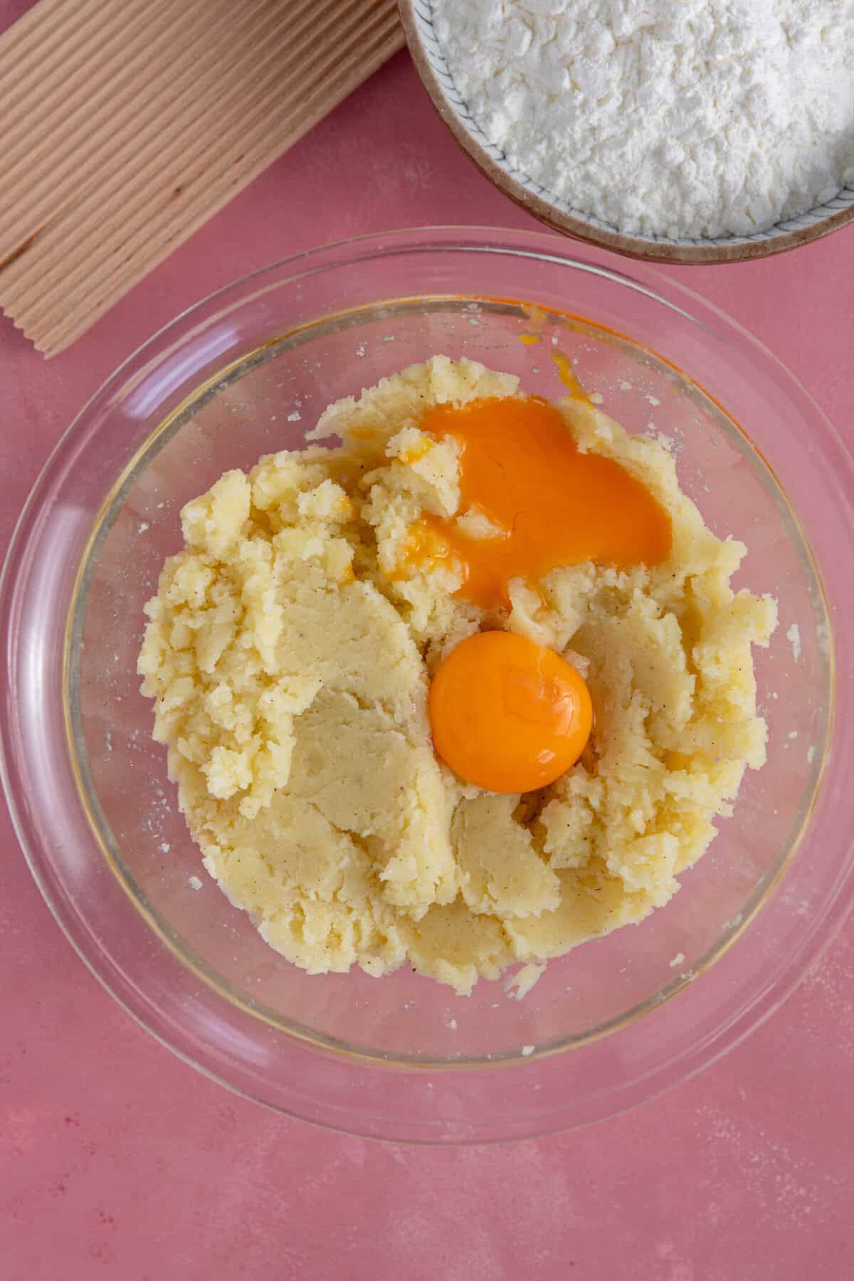 Process shot of gluten free gnocchi recipe showing the egg yolks added to the mashed potato in a glass bowl.