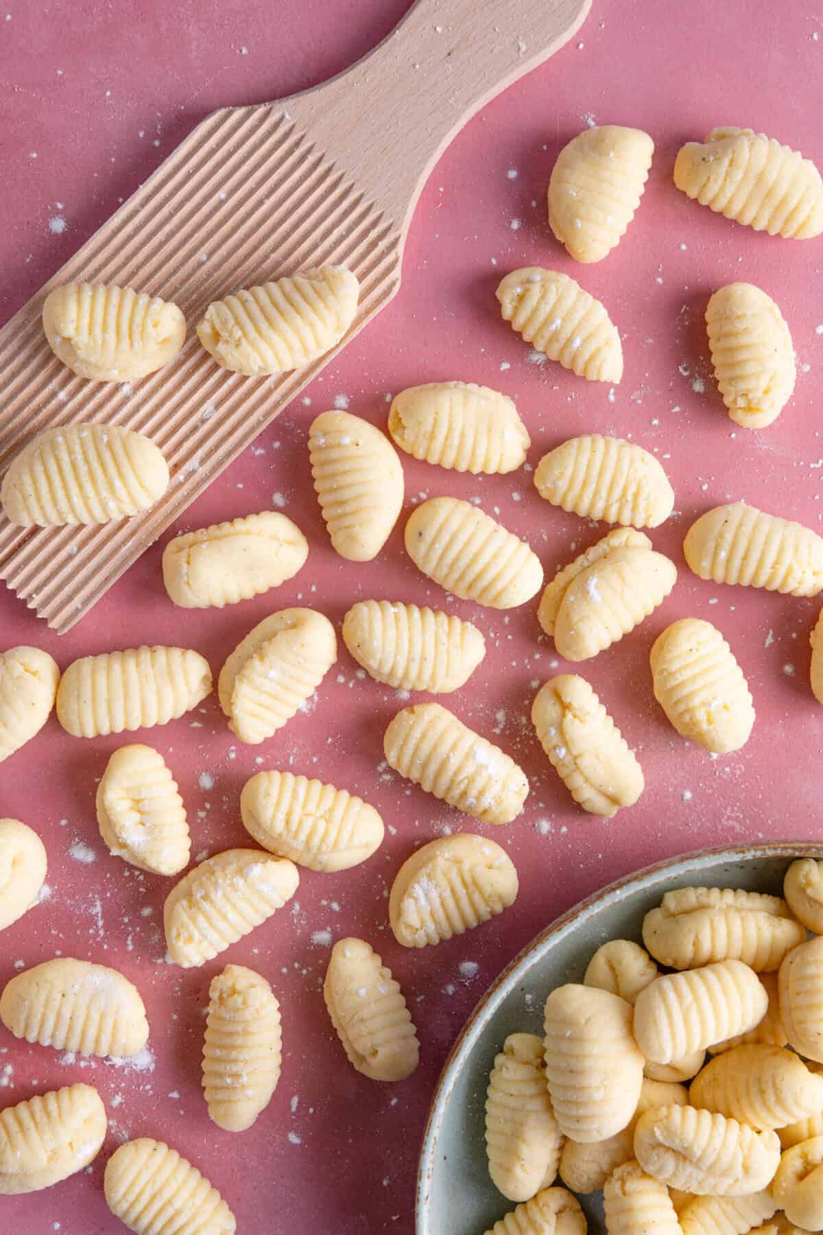 Overhead shot of gluten free gnocchi with a gnocchi board, on a pink work surface.