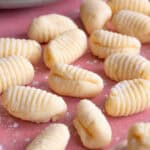 Close up shot of gluten free gnocchi on a pink worktop.