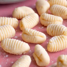 Close up shot of gluten free gnocchi on a pink worktop.