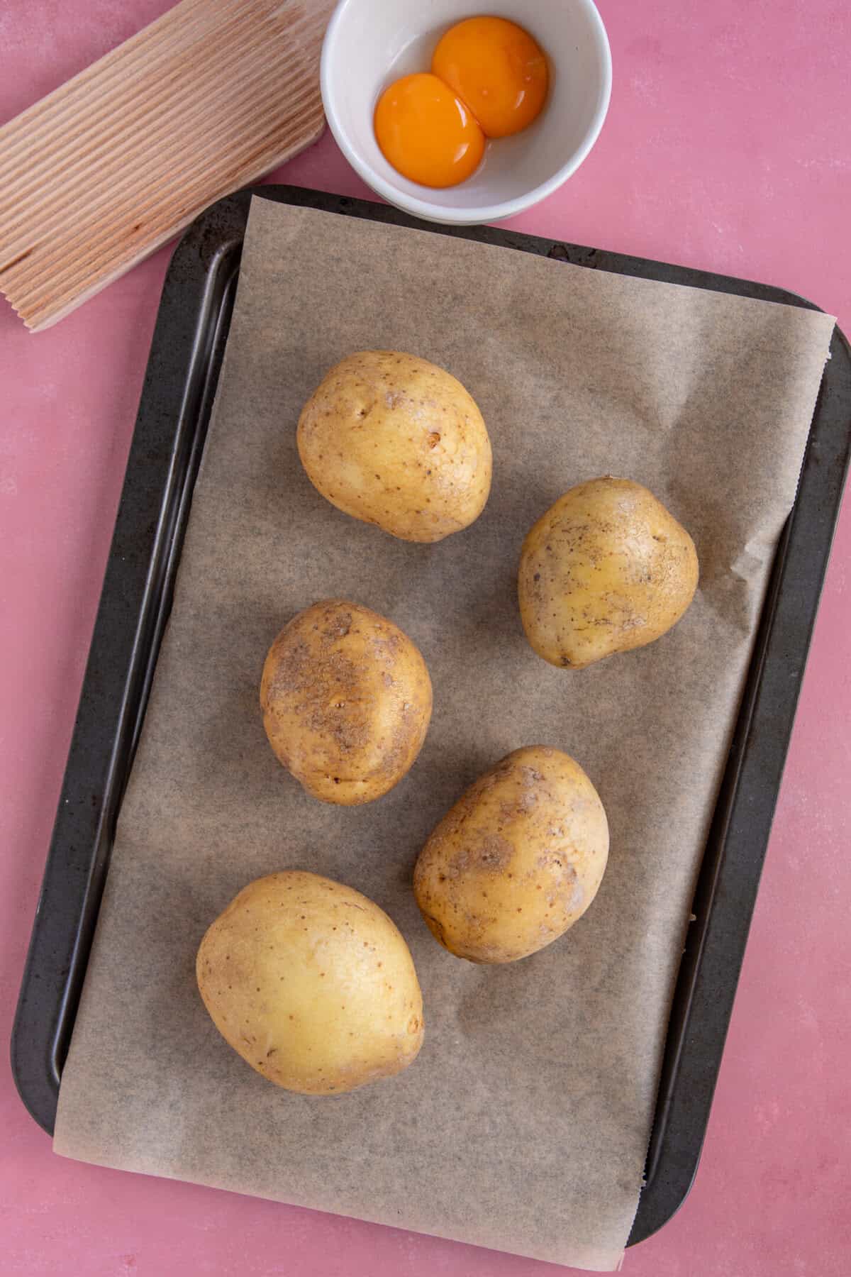Process shot of gluten free gnocchi recipe showing the potatoes on a lined baking sheet ready to bake.