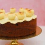 A gluten free simnel cake on a gold cake stand with a pink backdrop.