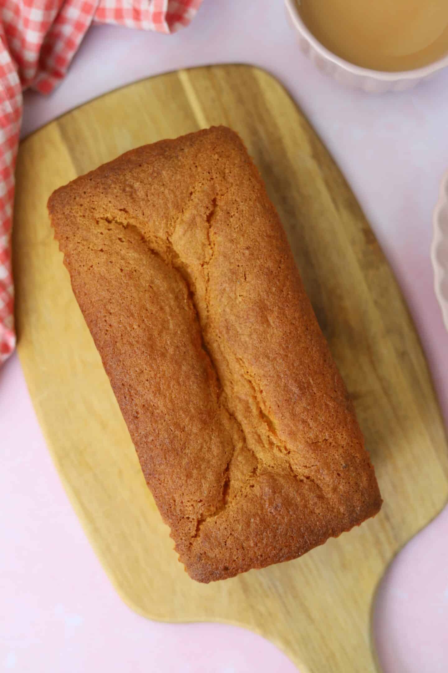 An uncut gluten free Madeira cake on a wooden chopping board.