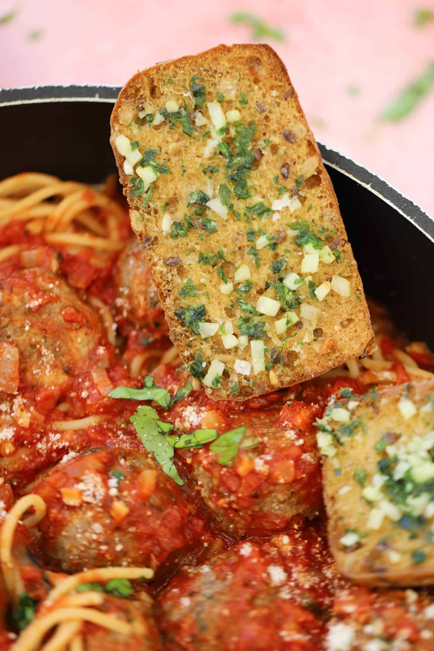Gluten free garlic bread on the side of a plan of meatballs.