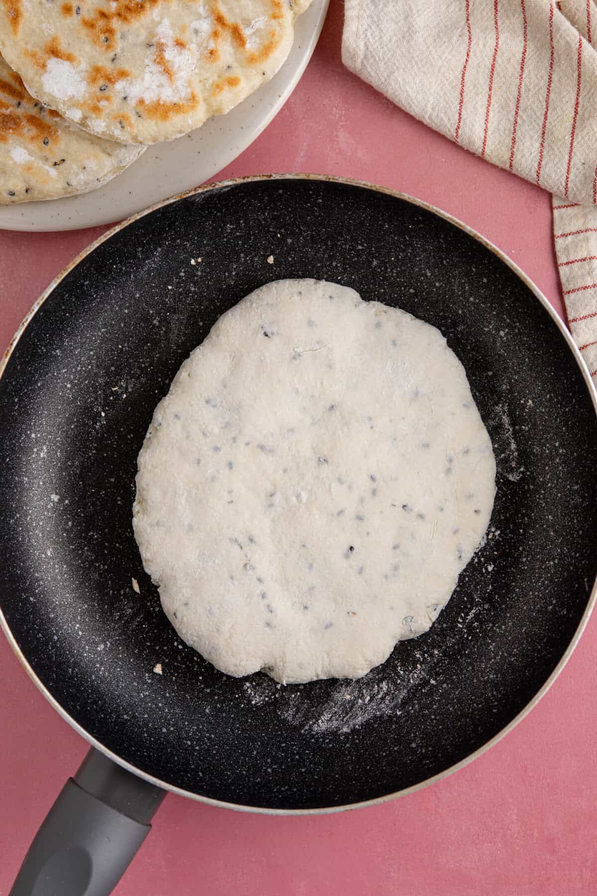 Process shot for gluten free naan bread recipe showing the naan bread cooking in a pan.
