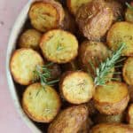 A bowl of crispy air fryer baby potatoes with a sprig of rosemary.
