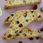 Gluten free biscotti on a pink backdrop with pistachios and cranberries.