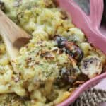 A pink dish filled with mac and cheese with pigs in blankets and sprouts.