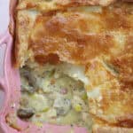 A gluten free chicken and ham pie in a pink pie dish with a portion taken out.