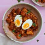 A bowl of chicken sausage pieces, beans and potatoes with a boiled egg on top.