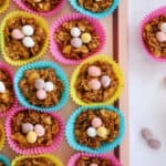 A pink tray of cornflake cake easter nests in colourful cake cases, topped with Mini Eggs.