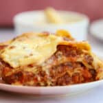 Close up of a portion of gluten free lasagne on a plate, showing the layers of pasta, cheese sauce and meat sauce.