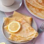 A plate of gluten free crêpes with lemon and sugar, with a cup of tea in the background.