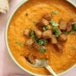 A bowl of gluten free carrot and lentil soup with croutons on top.