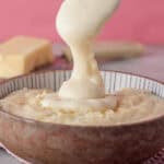 A spoon drizzling gluten free white sauce into a bowl.