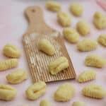 Gluten free gnocchi on a gnocchi board, on a pink work surface.