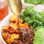 A spoon pouring honey onto a bowl of ground beef, sweet potatoes, avocado and broccolini.