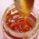 Hot honey being drizzled into a jar from a spoon.