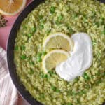 A pan of pea risotto with creme fraiche and lemon on top.