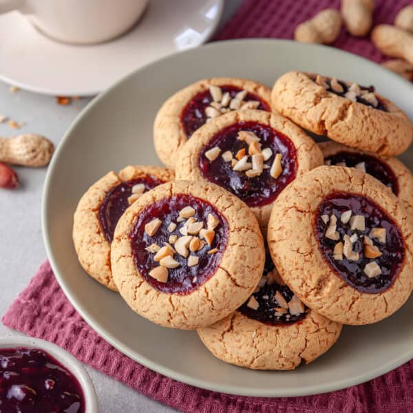 A plate of peanut butter jelly cookies with a cup of tea behind.