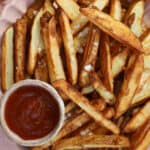 A pink bowl filled with air fryer chips and a small dish of tomato ketchup.