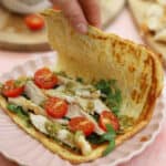 A hand folding a cottage cheese flatbread over a filling of chicken, tomato and rocket.