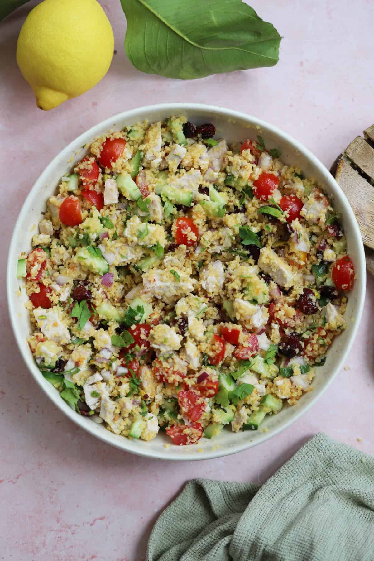 A bowl of couscous salad with turkey, tomato, cucumber, pistachios and cranberries.