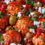 Close up shot of a pan of Greek chicken meatballs with olives and feta.