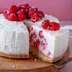 A raspberry and white chocolate cheesecake with a slice taken out of it.