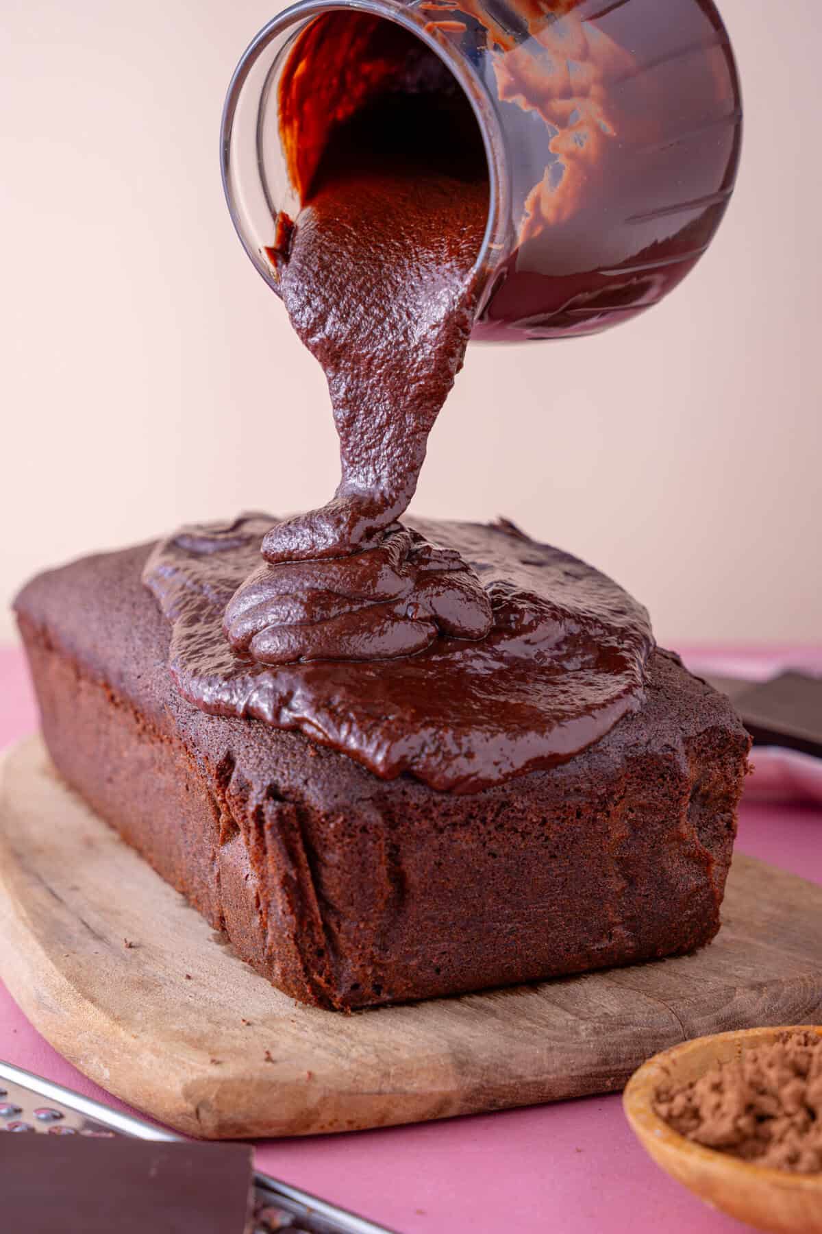 A jug of chocolate ganache poured onto a loaf cake.
