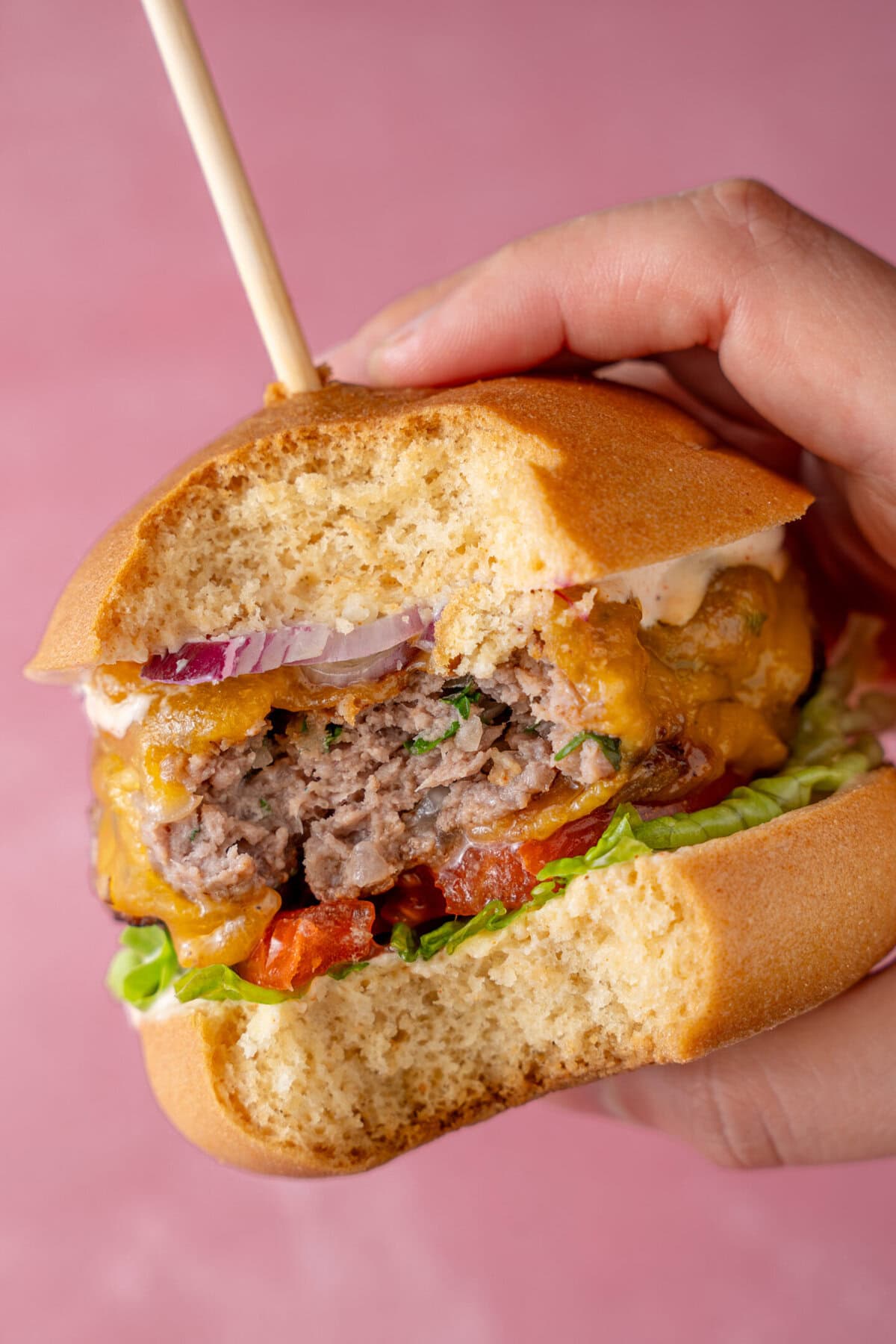 A hand holding a gluten free beef burger with a bite taken out.