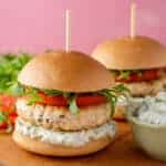 Two Greek chicken burgers in gluten free buns served with tzatziki.