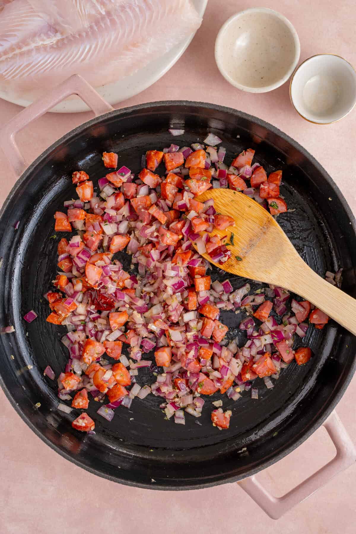 Frying chorizo, herbs and red onion in a pan.