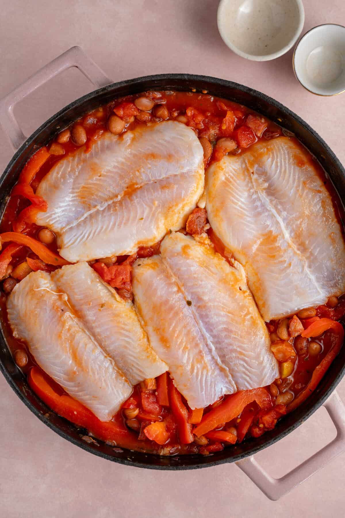 The fish fillets nestled into the tomato sauce to cook.