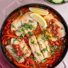 A pan of cod and chorizo stew served with lemon wedges and salad.