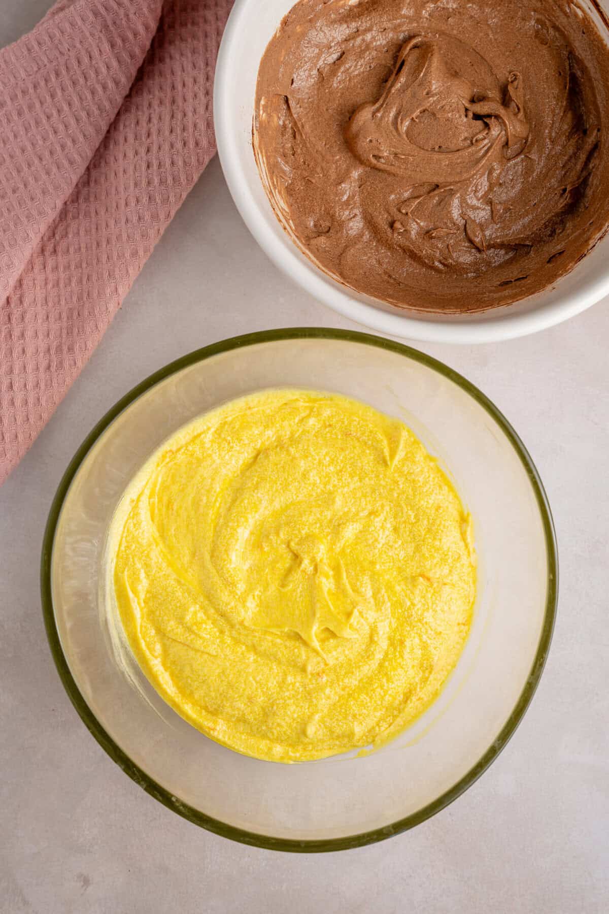 A bowl of orange cake batter and a bowl of chocolate cake batter.