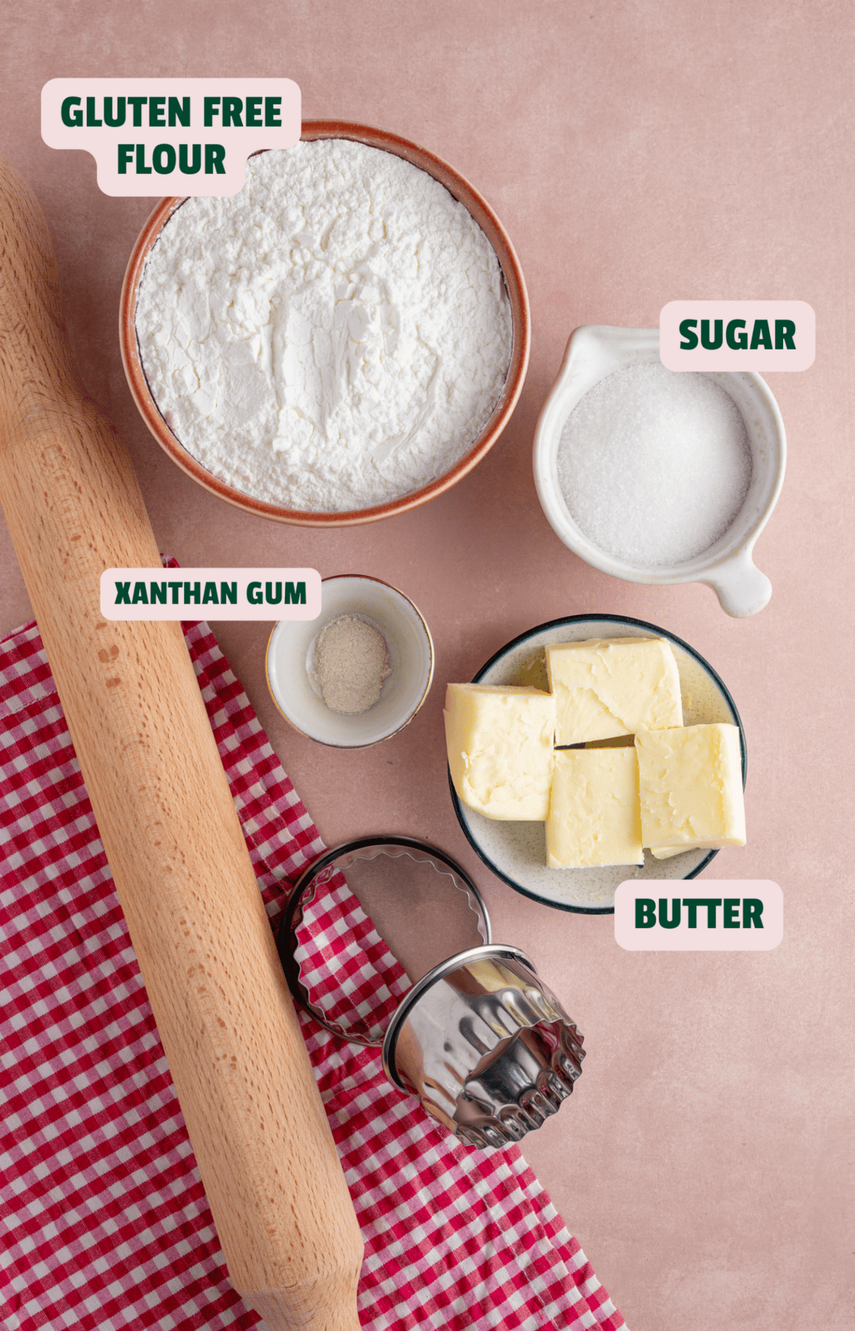 Ingredients for gluten free shortbread with text labels, alongside a rolling pin and biscuit cutters.