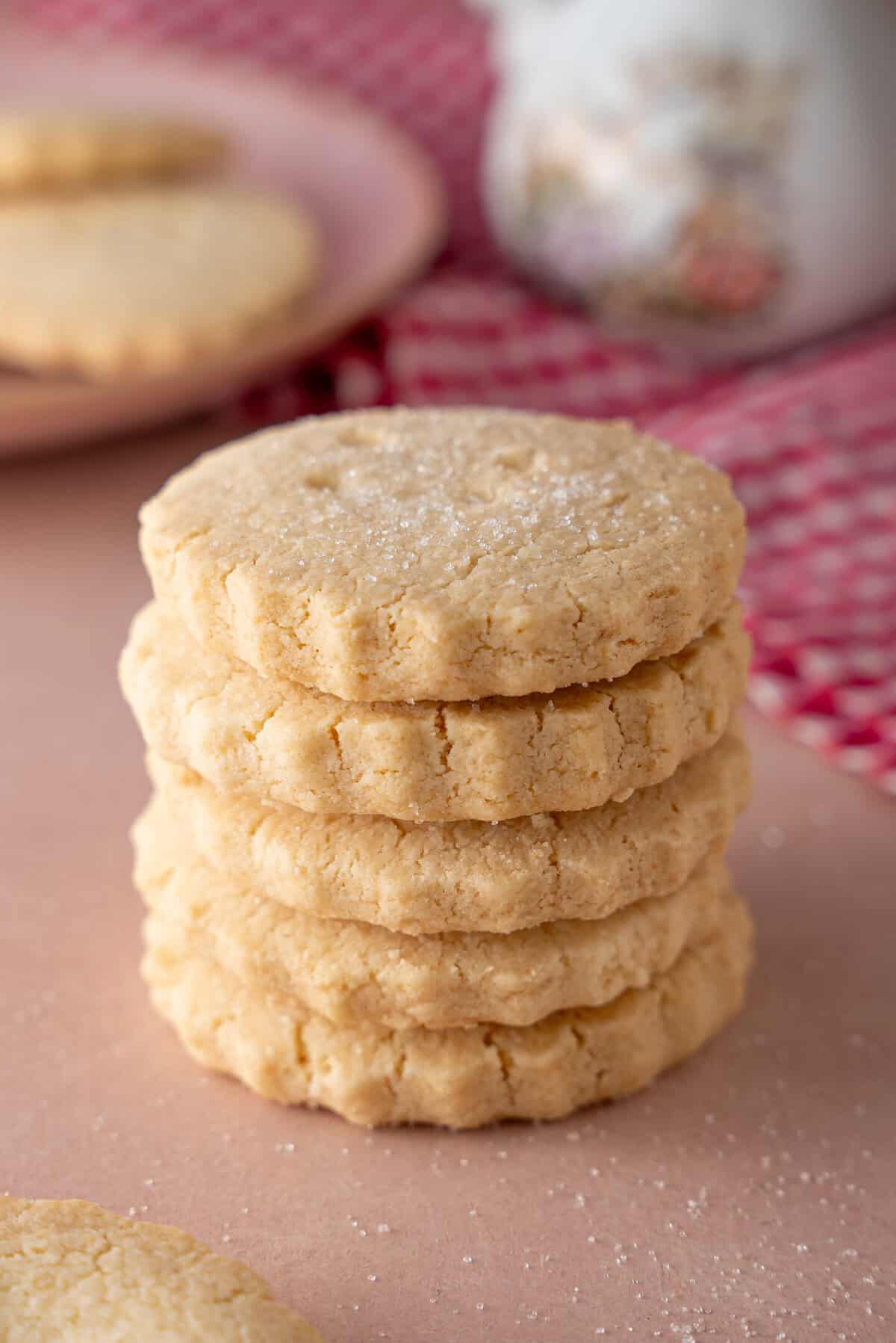 A stack of gluten free shortbread biscuits on a pink worktop.