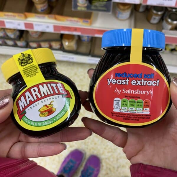 Hands holding a jar of marmite and a jar of Sainsbury's yeast extract.
