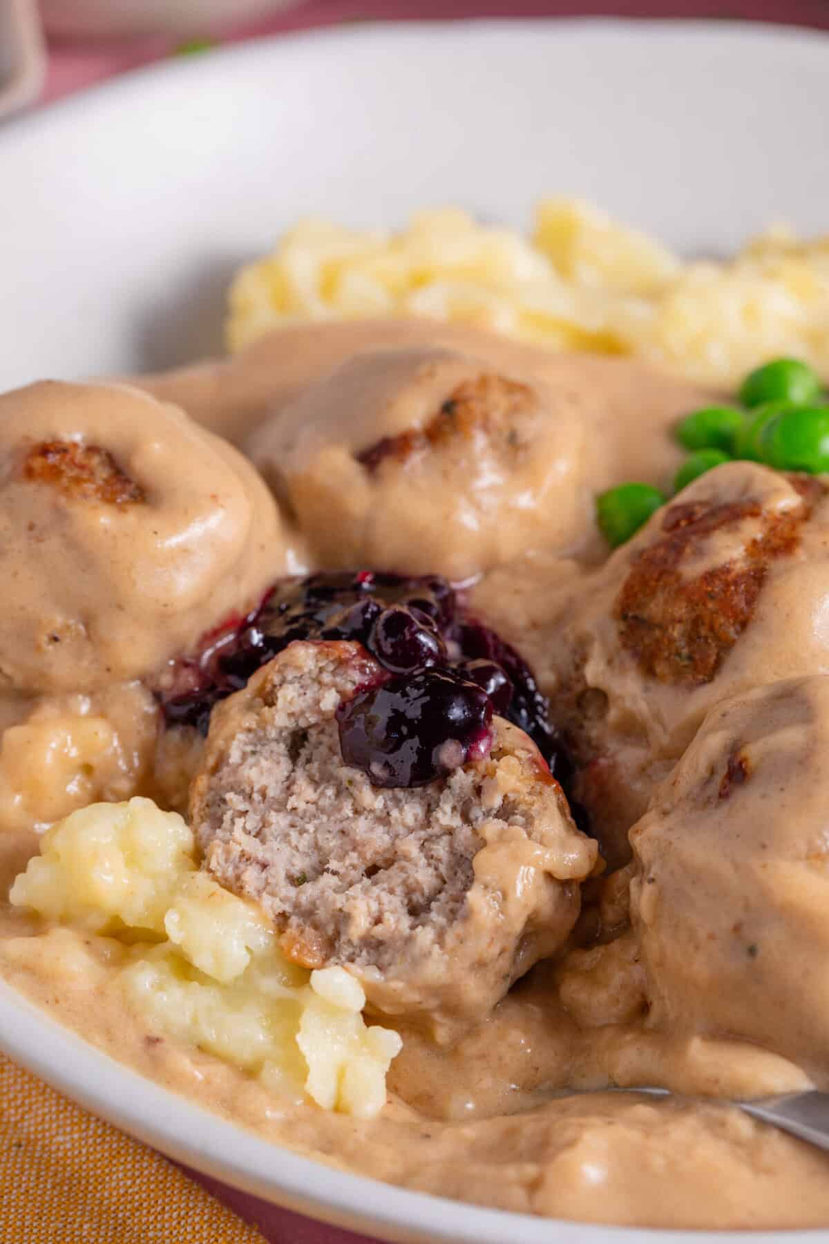 Close up of gluten free Ikea meatballs cut in half with mash and cranberry sauce.