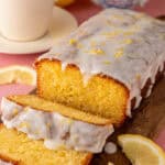 A gluten free lemon drizzle cake cut into slices with a cup of tea behind.