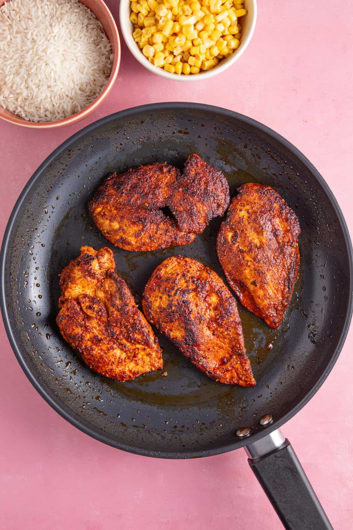 Chicken breasts coated with spiced in a frying pan.