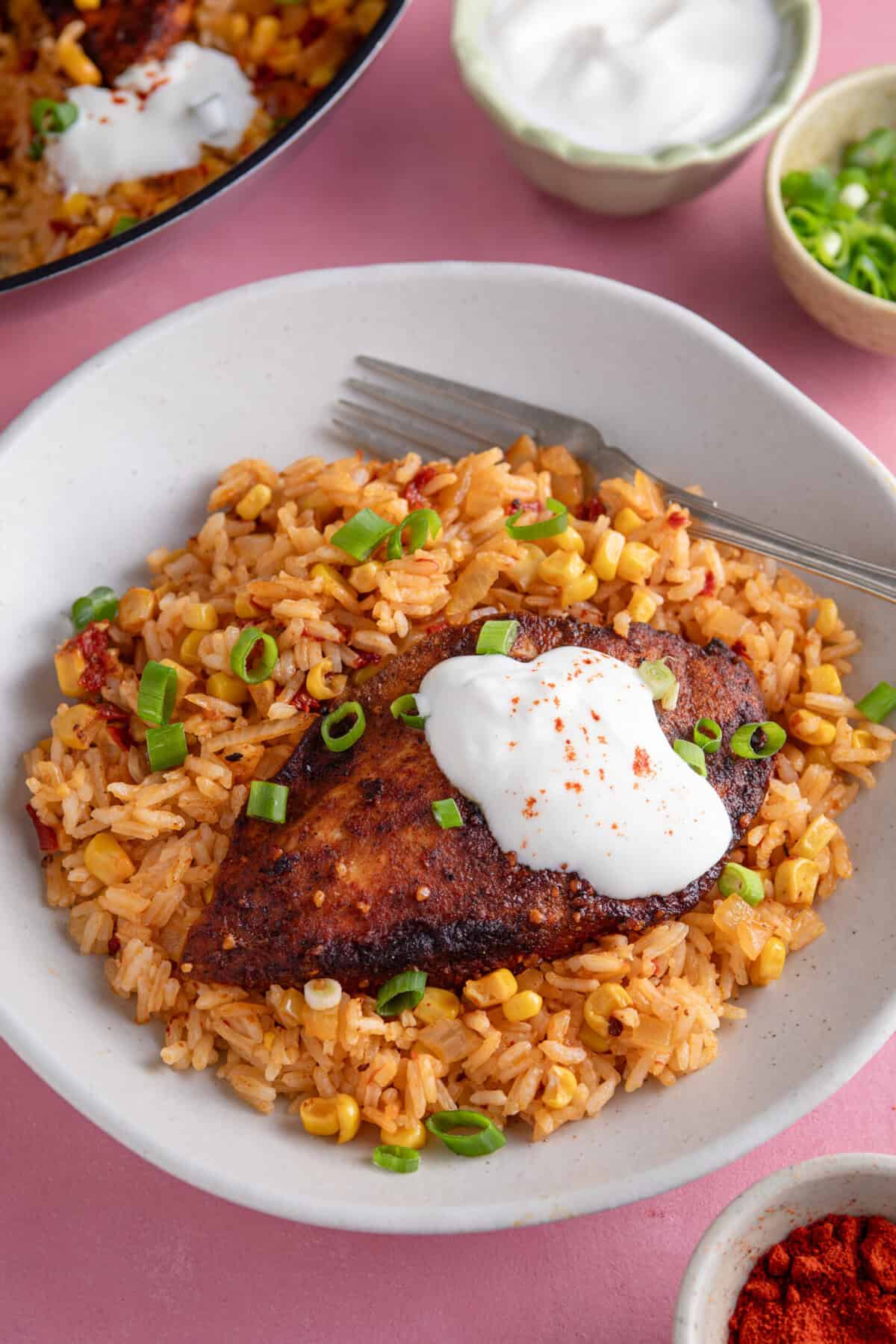 A plate of spicy rice with a chicken breast and soured cream.
