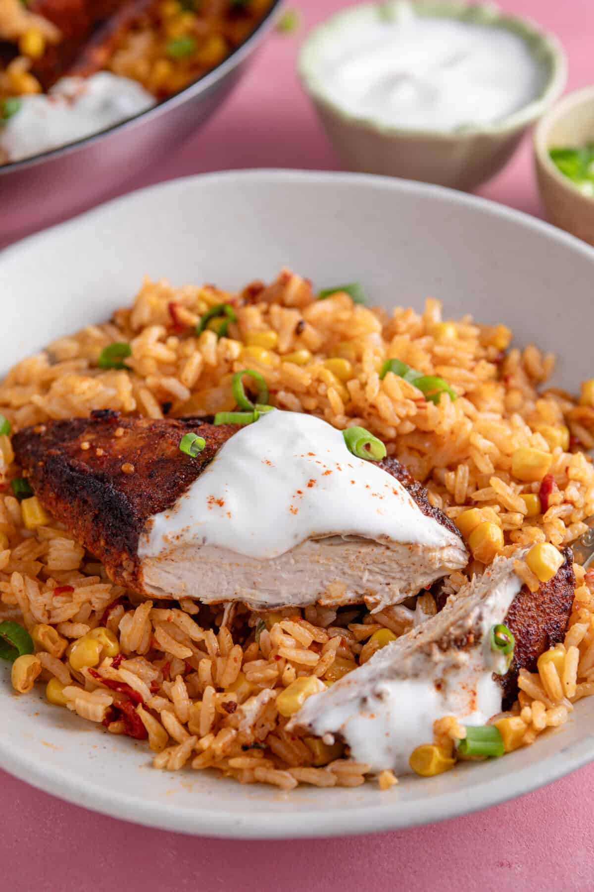 A plate of spicy rice with a chicken breast and soured cream.