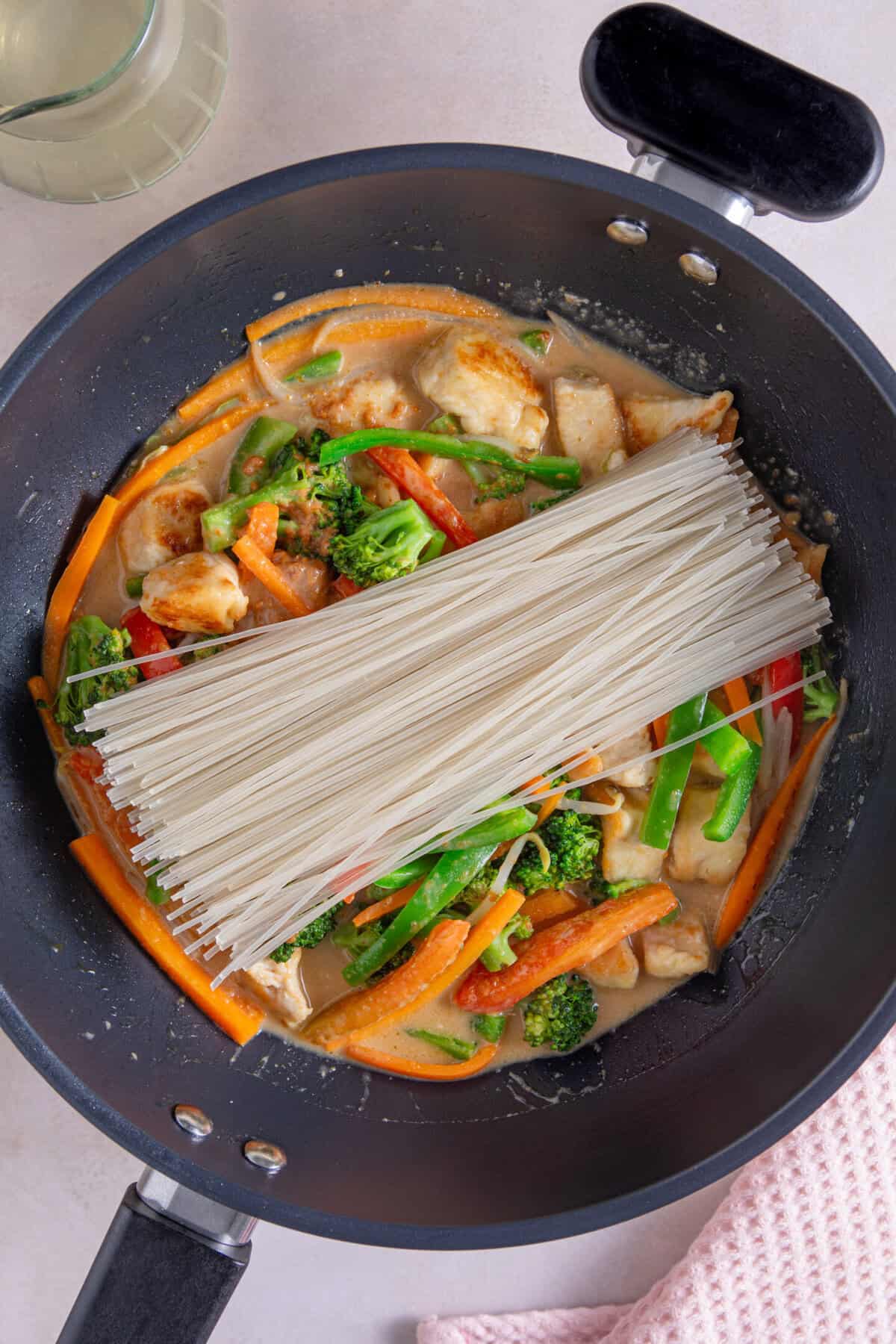 Add the dry rice noodles and the peanut butter sauce to the pan.