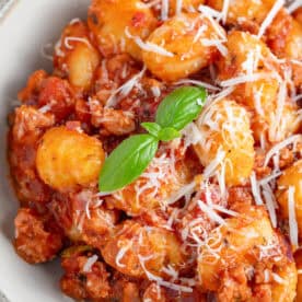 A bowl of sausage gnocchi bake with cheese and basil on top.